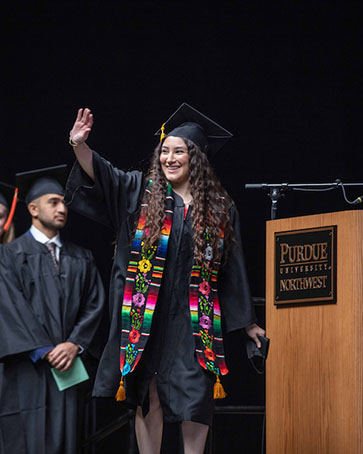A PNW graduate waves on stage