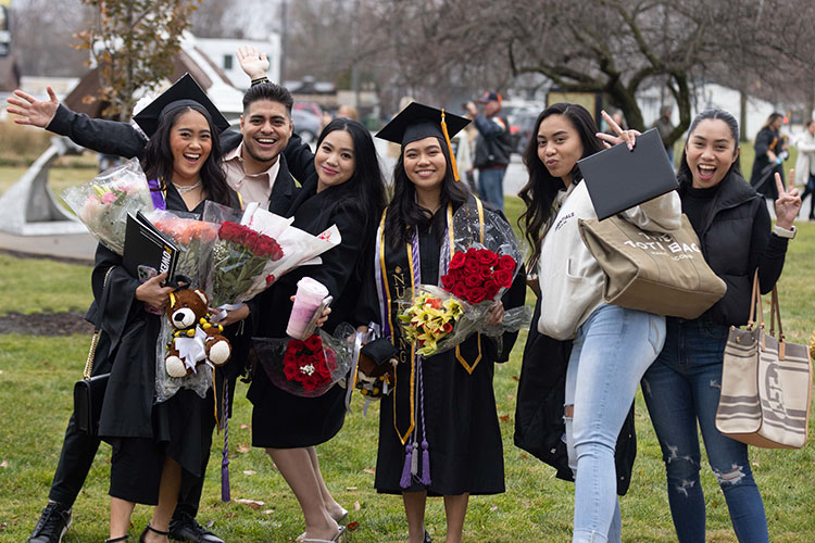 Graduates pose after commencement with flowers and degrees