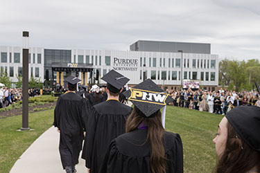 PNW graduates in the procession at spring 2023 commencement. A mortar board decorated with PNW is visible, as is the Nils K. Nelson Bioscience Innovation Building in the background.