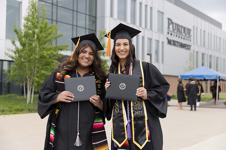 Two PNW graduates hold their diplomas in front of the Nils K. Nelson Bioscience Innovation Building at spring 2023 PNW commencement.
