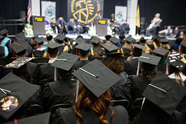 Rows of students facing the stage during an indoor commencement ceremony. Everyone is wearing black commencement regalia.