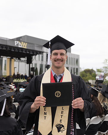 A PNW student athlete poses with their degree holder during commencement