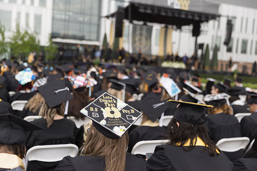 Students sit outside in commencement regalia.