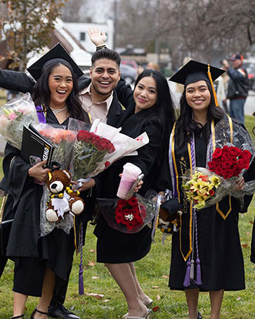 Graduates pose after commencement with flowers and degrees