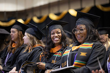 Four students sit in a line of seats during the fall 2023 commencement ceremony.