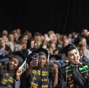 Three students pose with their phones in the air