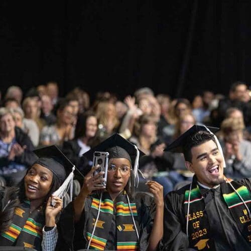 Three students pose with their phones in the air