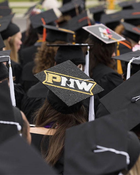 A cap decorated with PNW in the midst of a group of Purdue Northwest graduates at Commencement.
