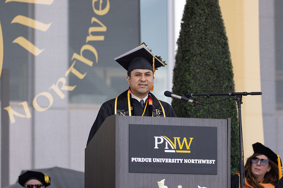 PNW student speaker Felipe Oria stands on stage and speaks into a microphone