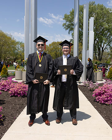 Two graduates pose together under the bell tower