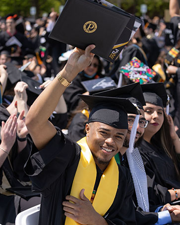 Graduate celebrates by raising diploma into the air.
