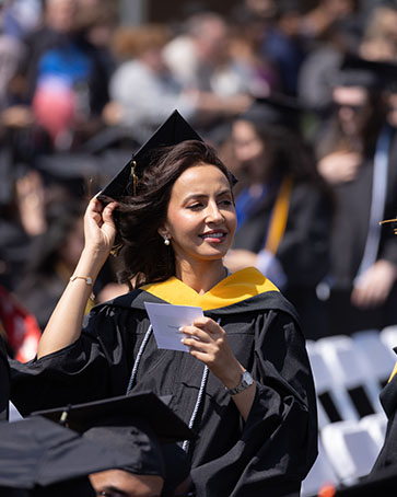 Graduate adjusts cap while looking out to the crowd during commencement.