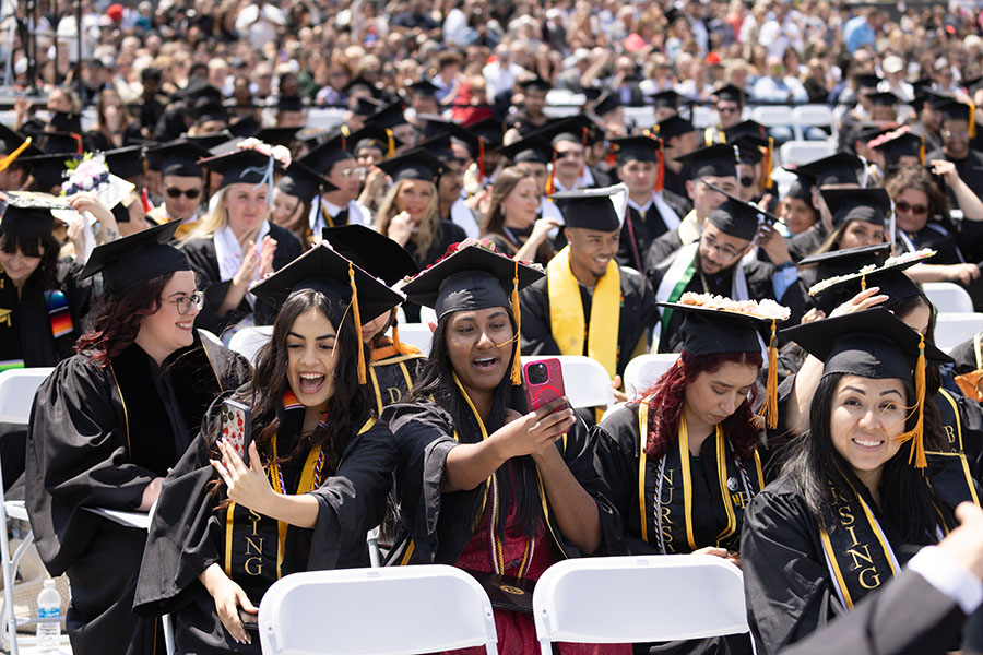 Graduates take selfies and sit in the crowd during commencement