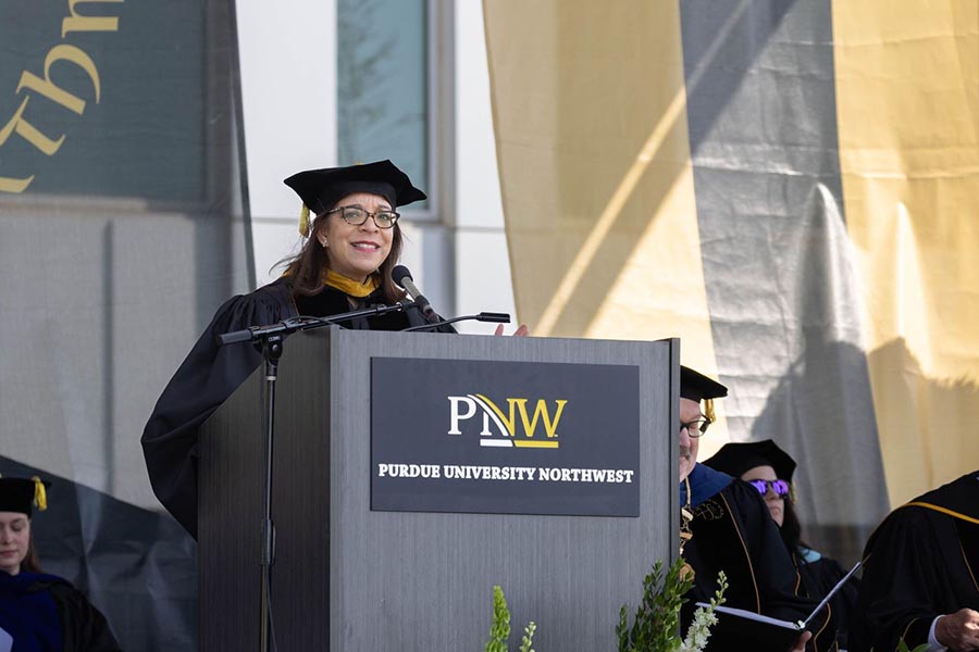 A woman in graduation regalia speaks at a Purdue University Northwest podium.
