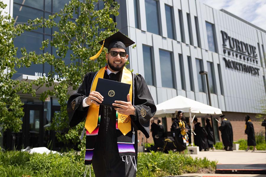 A PNW graduate holds his diploma in front of the Nils K. Nelson Bioscience Innovation Building