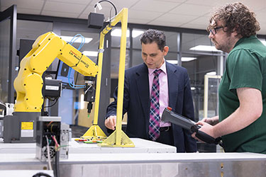PNW Professor Maged Mikhail works with a student on a yellow mechatronics machine.