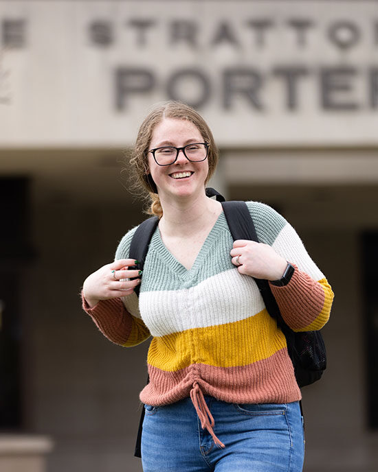 A student stands out doors with the Porter building behind them.