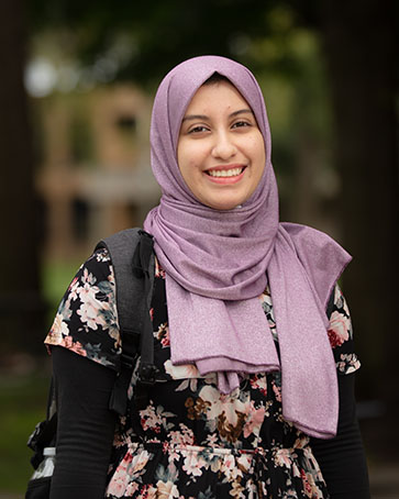 A student stands outside and smiles at the camera