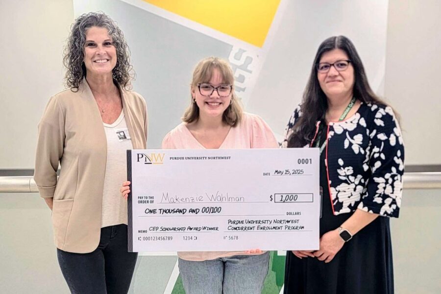 Three people stand together. The person in the middle is holding up a scholarship check.