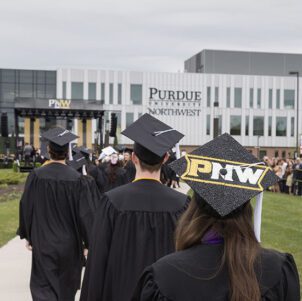 PNW graduates in the procession at spring 2023 commencement. A mortar board decorated with PNW is visible, as is the Nils K. Nelson Bioscience Innovation Building in the background.