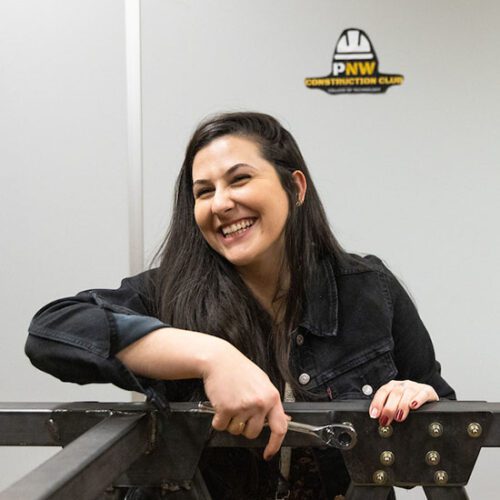 A student in a black denim jacket turns a wrench and smiles