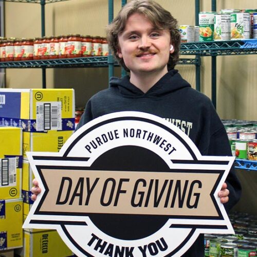 A student in the PNW Food Pantry holds a Purdue Northwest Day of Giving "Thank You" sign.