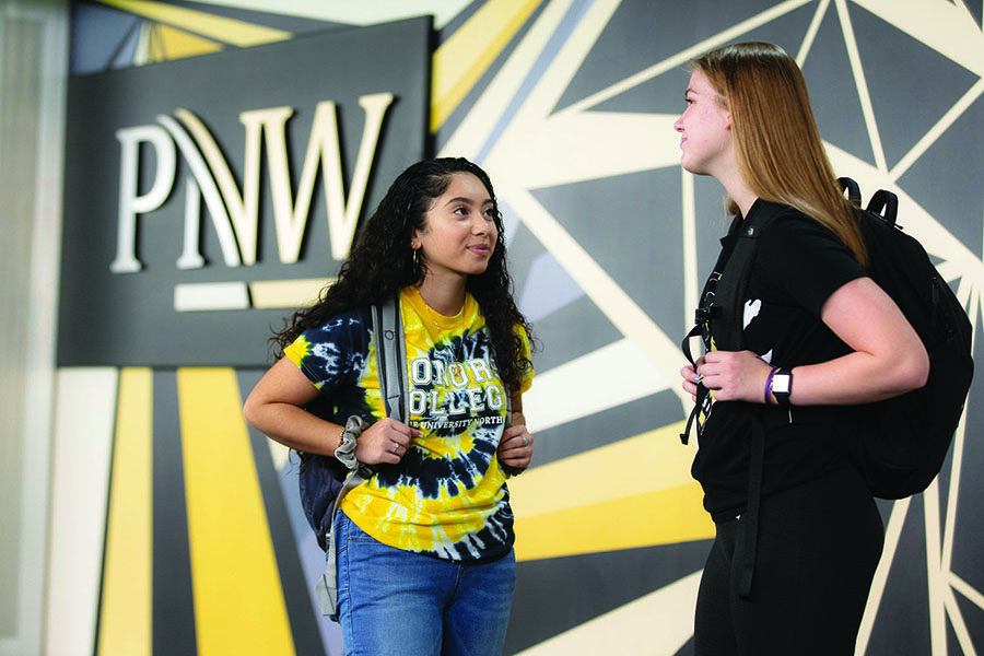 Two students talking while standing in front of a PNW mural