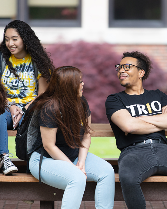 Three students sitting on a picnic table and smiling