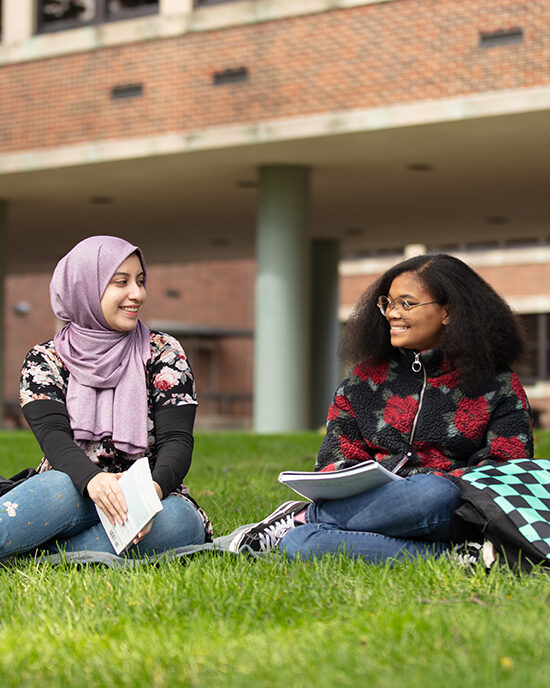 Two students sit outside with books