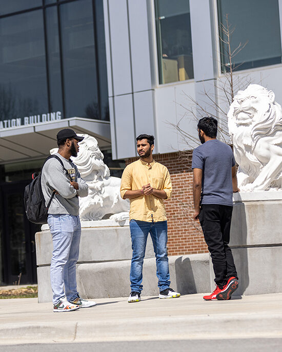 Three students standing around lion statues on the Hammond Campus