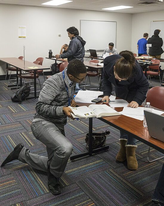 A professor kneeling to help a student at a desk