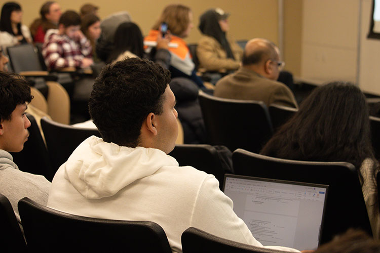 PNW students, faculty and staff sit in a lecture hall. They are pictured from the back.