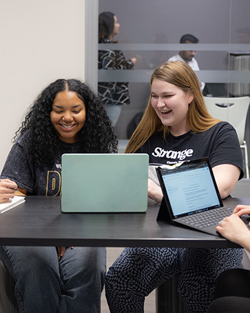 Two students sit at a table and work on a laptop.