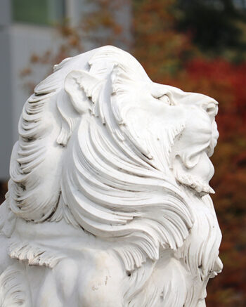 A lion sculpture in front of fall foliage