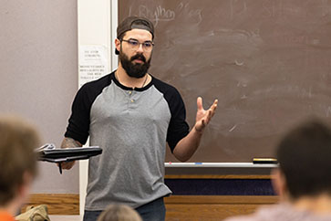 A PNW student stands in front of a classroom.