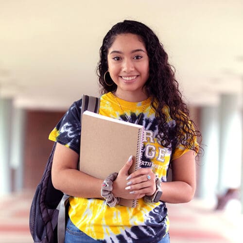 A PNW student in a tie-dye t-shirt holds her notebook outdoors.