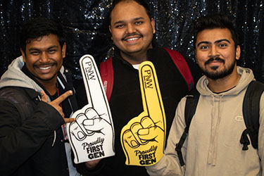 Three students pose together. Two of the students are holding up "Proudly First-Gen" foam fingers