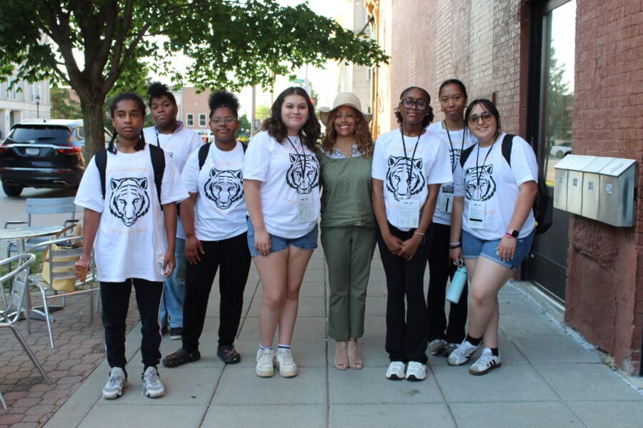 a group of 7 high school boys and girls taking a photo with a middle aged woman