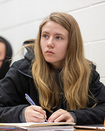 A student sis at a table and writes in a notebook