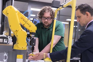 A PNW student working with a robot arm with a professor 363x242