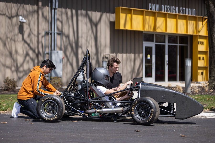 Three students work on a car outside of the PNW Design Studio