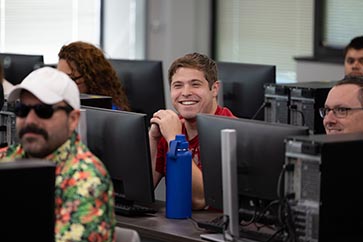 Students working on computers in class, while a student is smiling 363x242