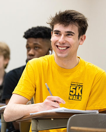 A student sits at a desk and writes in a note book