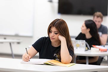 Female student writing in a notebook on a desk 363x242