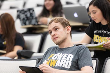 PNW student sitting in a chair while writing and taking notes on his iPad 363x242