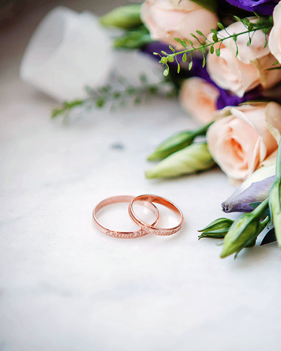 Two wedding rings on a marble table next to a bouquet of flowers.