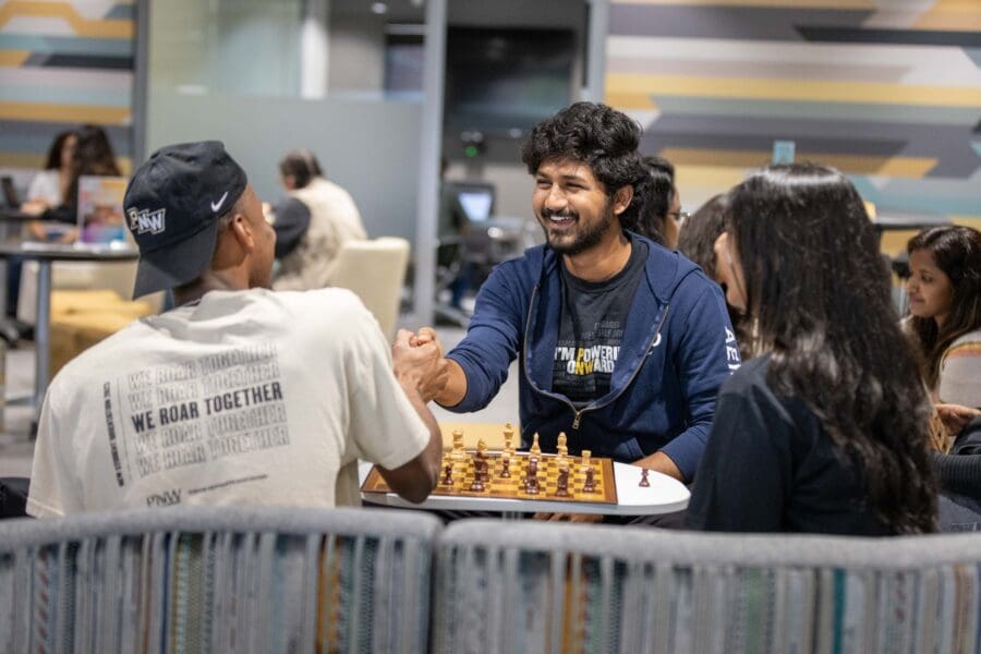 Three students gather around a chess game.