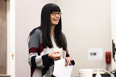 Erin Okamoto Protsman holds a stack of papers during a class.