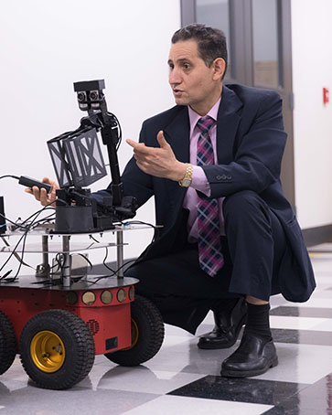 Maged Mikhail kneels on the ground next to a machine.