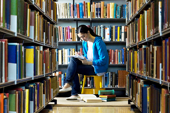 Student surrounded by books in a library